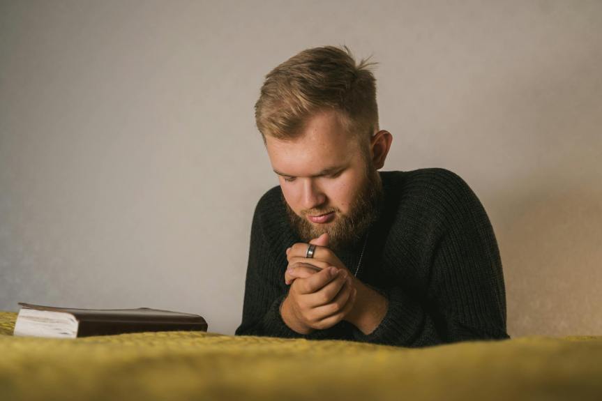 close up shot of a bearded man in black knitted sweater praying