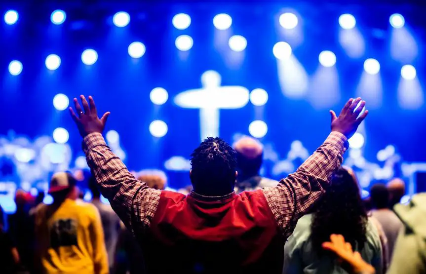 photo of a man raising his hands towards a stage with a cross
